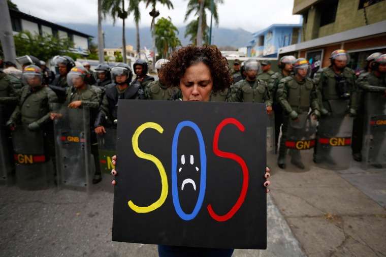 Image: A demonstrator holds a placard as she stands in front of national guards during a protest near the Cuba's Embassy in Caracas