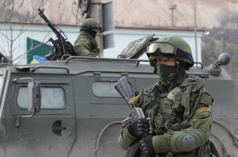 Image: Armed servicemen wait in Russian army vehicles outside a Ukranian border guard post in the Crimean town of Balaclava