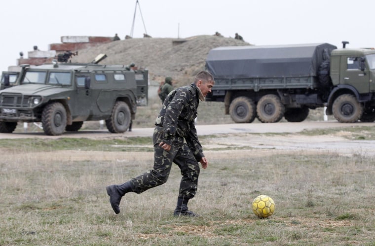 Image: A Ukrainian serviceman kicks a soccer ball near Russian military vehicles at the Belbek air base in the Crimea region