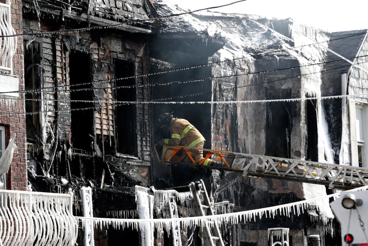 Image: A firefighter inspects a charred home while standing on a ladder from a fire truck in Jersey City, N.J.