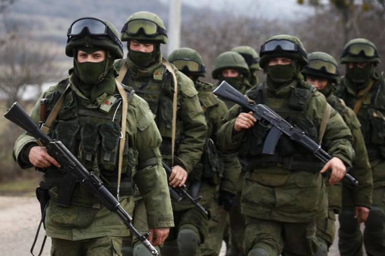 Image: Armed men, believed to be Russian servicemen, march outside an Ukrainian military base in the village of Perevalnoye