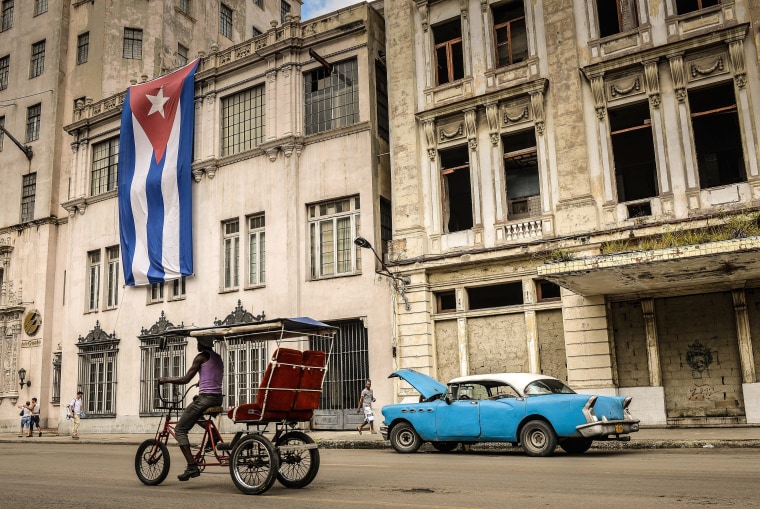 A bike-taxi and a vintage American car are seen in front of a building decorated with a large Cuban flag, on December 31, 2013, in Havana. 