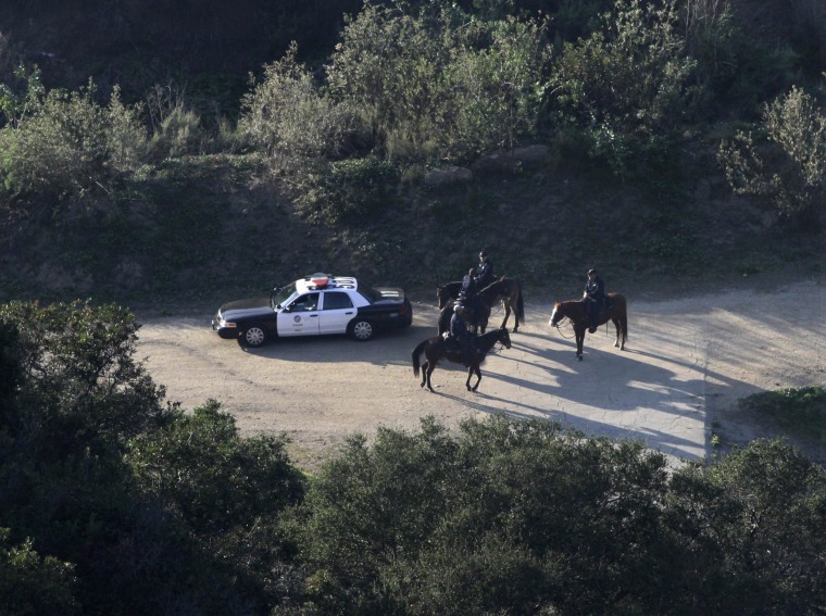 Image: LAPD mounted police officers search a hilly area below the iconic Hollywood sign in Los Angeles