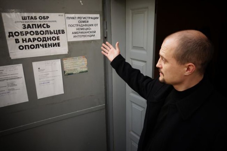 Alexei Borsuk gestures toward signs in the PLM offices. The sign on the right says, "Registration point for families suffering from the German-American intervention." With a smile, Borsuk adds: "I politicized that one a bit."