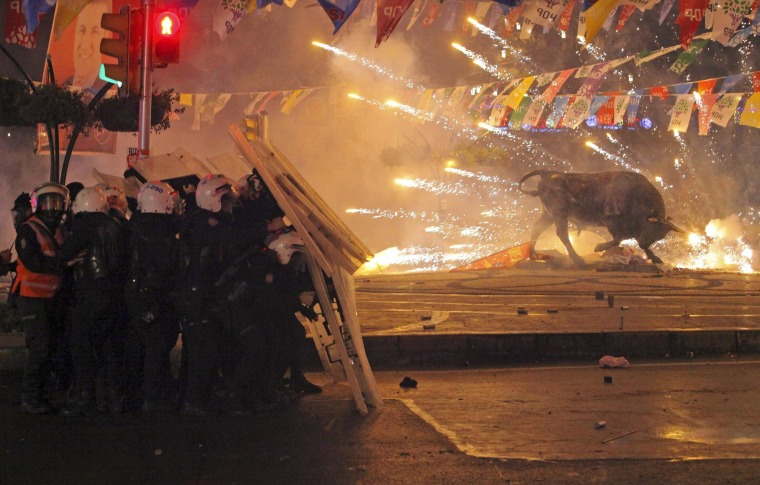 Image: Riot policemen shield themselves as fireworks thrown by protesters explode next to the statue of a bull, during an anti-government protest in Kadikoy