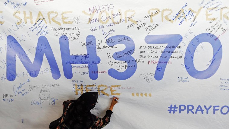 Image: Woman writes message of support and hope for passengers of missing Malaysia Airlines MH370 on banner at Kuala Lumpur International Airport