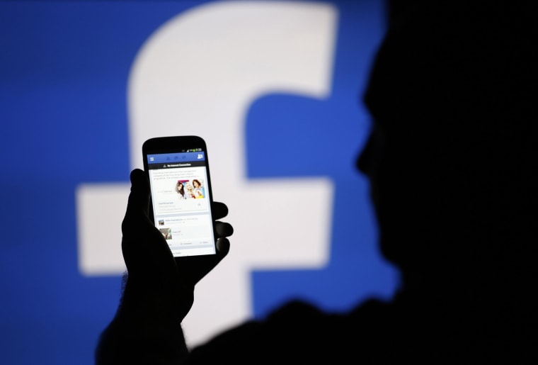 Image: A man is silhouetted against a video screen with an Facebook logo as he poses with an Samsung S4 smartphone in this photo illustration taken in the central Bosnian town of Zenica
