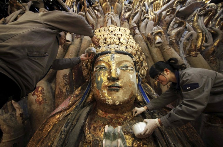 Image: Workers peel off loose gold foil as part of a restoration project for a Thousand-Hand Guanyin Buddhist statue in Chongqing