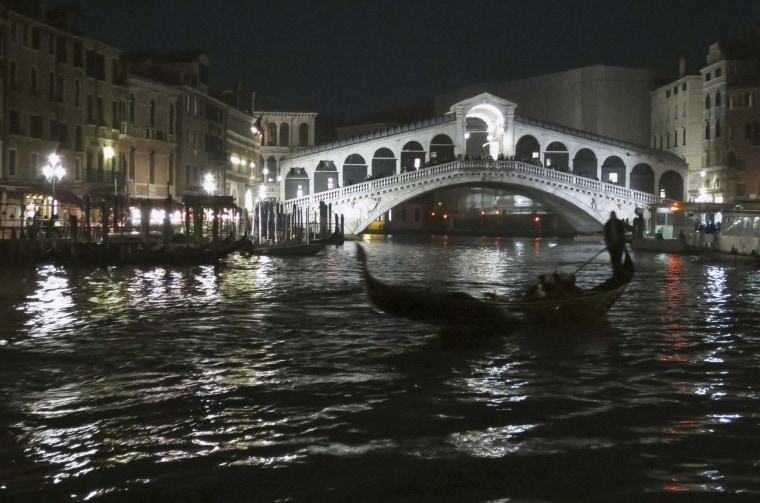 Image: A gondola passes along the Grand Canal in front of the Rialto bridge, in Venice
