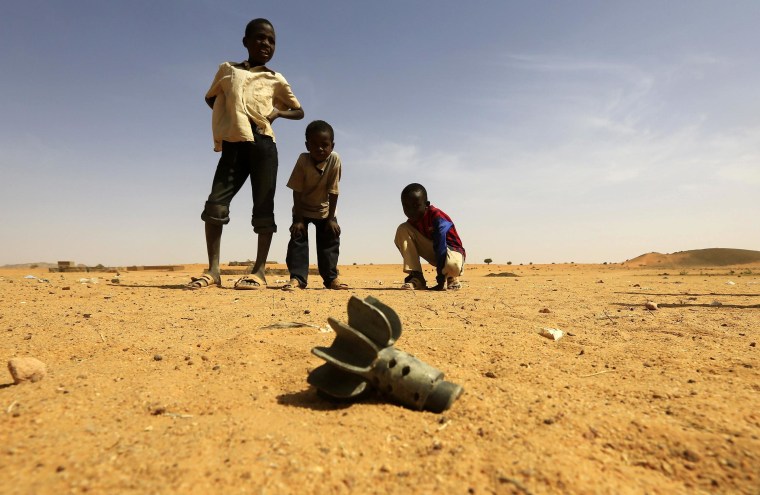 Image: Children look at the fin of a mortar projectile that was found at the Al-Abassi camp for internally displaced persons, after an attack by rebels, in Mellit town