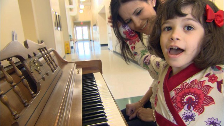 Kim Cristo sits at a piano with her daughter Ava, 6.  Kim credits the intervention Ava has received at REED Academy in Oakland, N.J., for helping her overcome some of the language deficits caused by autism.