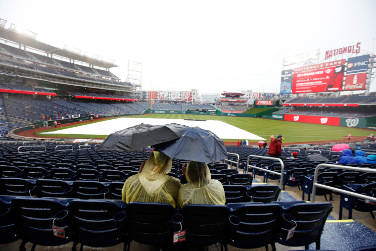Image: Fans sit under umbrellas in the rain before an exhibition baseball game between the Washington Nationals and the Detroit Tigers at Nationals Park Saturday