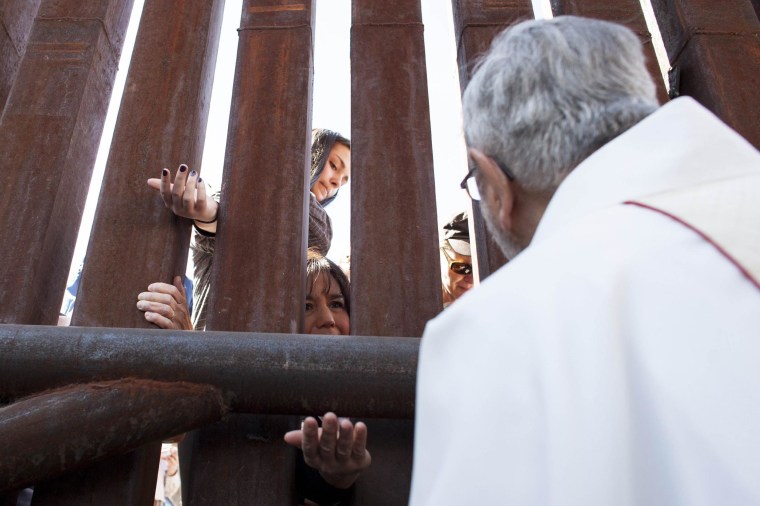 Image: Tucson Diocese Bishop Kicanas offers Holy Communion through the border to the Mexico side of the fence, during a special mass at the United States and Mexico border near Nogales