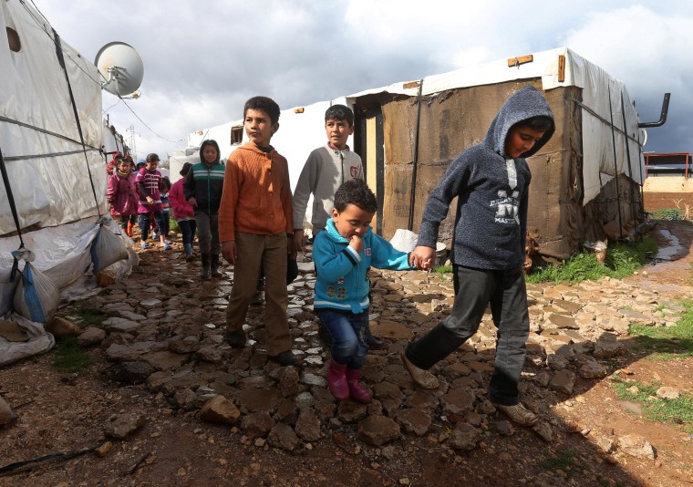 Image: Syrian refugee children walk between their tents on their way to a makeshift school