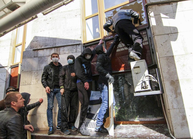 Image: Pro-Russia protesters attempt to enter through a broken window as they storm the regional government building in Donetsk