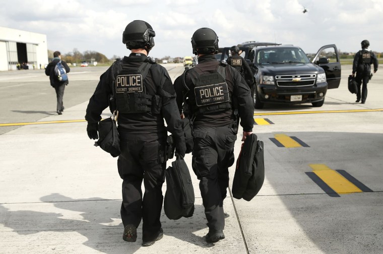 Image: Two Secret Service CAT team members walk toward their motorcade vehicle at Brussels Airport