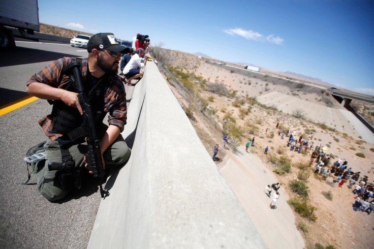 Image: An armed man stands watch as protesters gather by the Bureau of Land Management's base camp near Bunkerville, Nevada