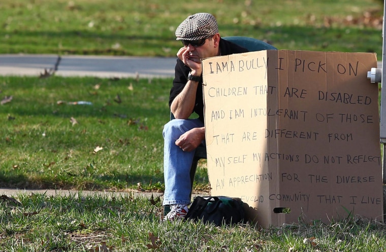 Image: Aviv sits with an "I am a bully" sign at a street corner in the Cleveland suburb of South Euclid