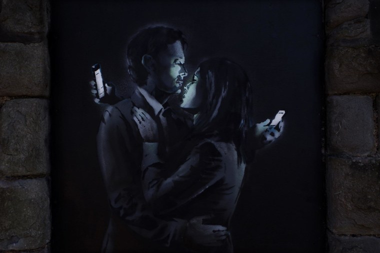 Banksy artwork depicting lovers looking at their cell phones.
