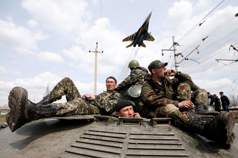 Image: A fighter jet flies above as Ukrainian soldiers sit on an armoured personnel carrier in Kramatorsk