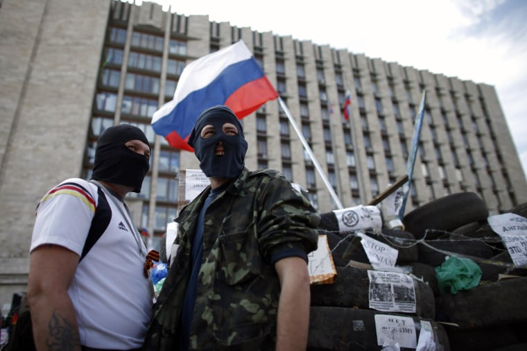 Image: Masked pro-Russia protesters stand guard near a barricade outside a regional government building in Donetsk