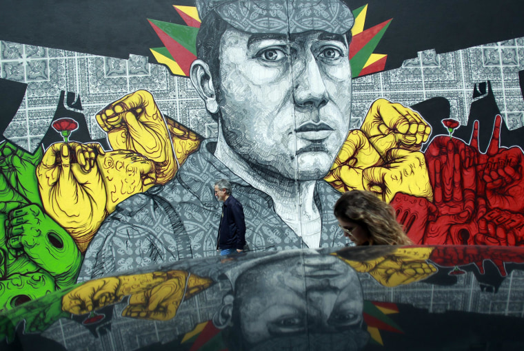 Image: People walk past a mural showing army captain Salgueiro Maia in Lisbon