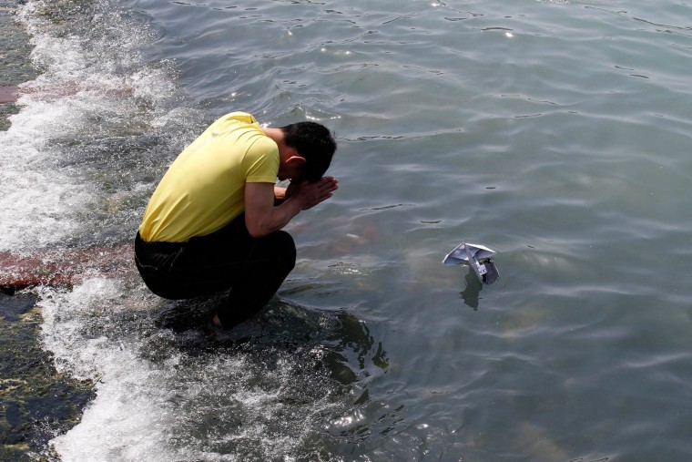 Image: Family member of a victim onboard capsized Sewol ferry, prays for missing and dead passengers, as he releases a paper boat with a message for them, at a port in Jindo