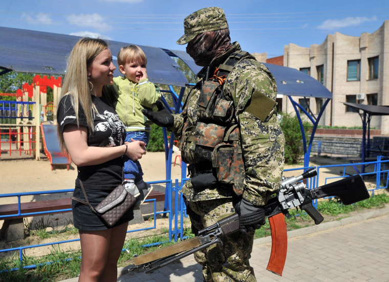 Image: A woman talks to an armed man in military fatigues