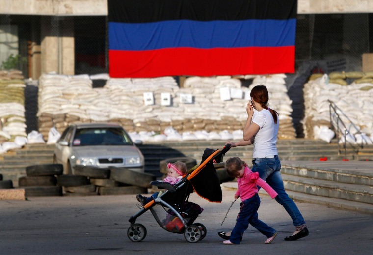 Image: A woman with children passes by barricades in Slaviansk