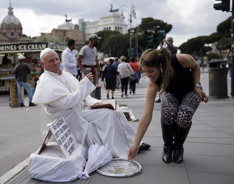 Image: A tourist drops a coins near Plisko Julius, a Slovakian man impersonating the late Pope John Paul II, after posing with him for a souvenir picture