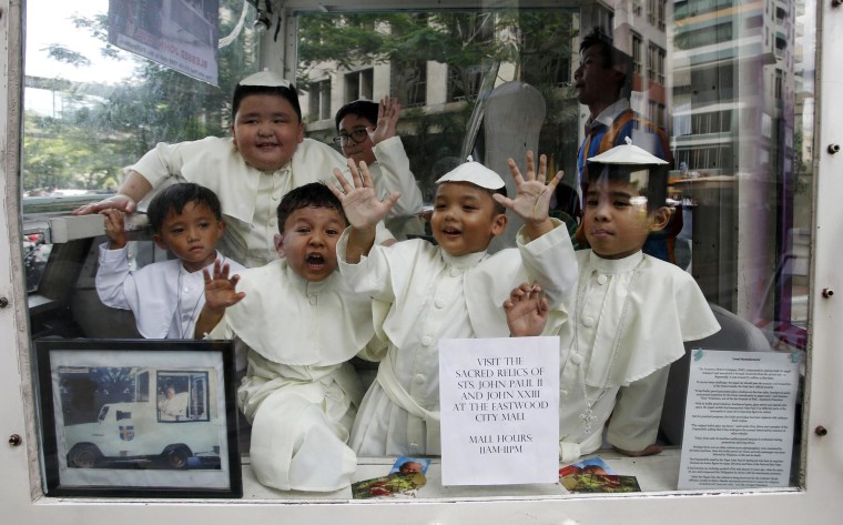 Image: Children wearing Pope's cassocks ride a Popemobile that was used by Pope John Paul II in his 1995 visit to Manila, during a parade in Quezon city