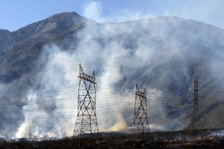 Image: Smoke rises near power lines with Cucamonga Peak in the distance at a wildfire in Rancho Cucamonga, California