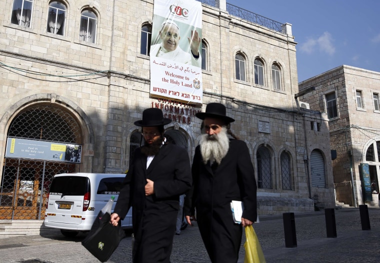 Image: Two Ultra Orthodox Jews walk past a large poster bearing the portrait of Pope Francis