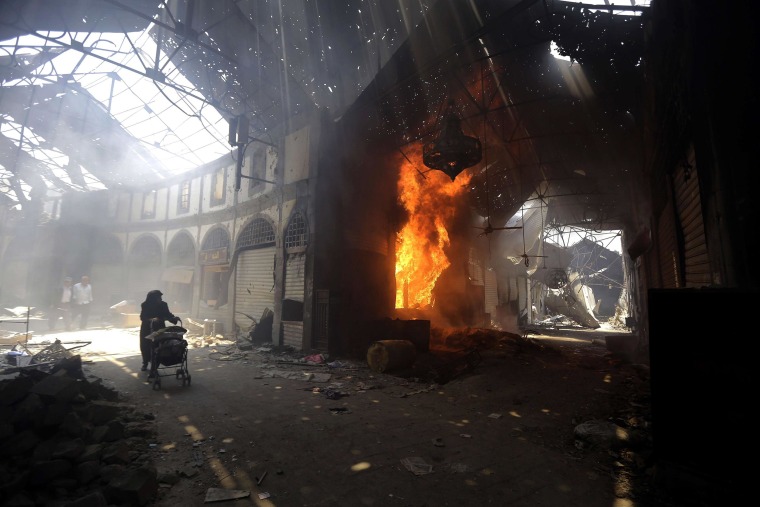 Image: A woman walks past a burning shop in the Maskuf market in the Old City of Homs