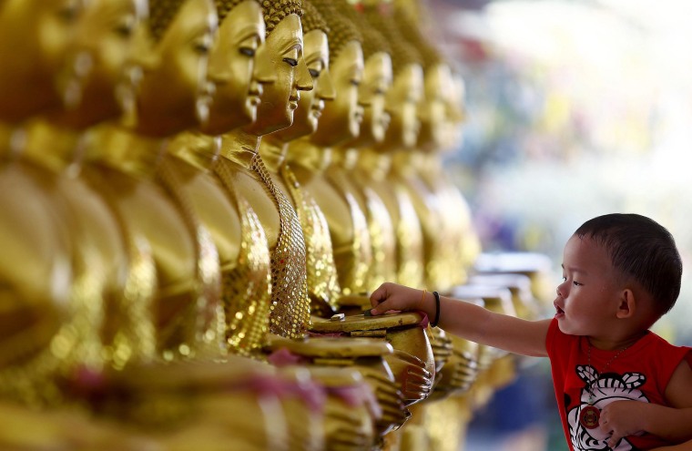 Image: A child drops coins into golden Buddha statues as a symbol of blessings on Vesak Day at the Thai Buddhist Chetawan Temple in Petaling Jaya