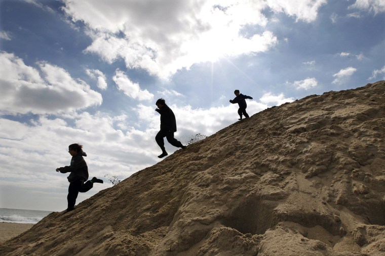 Image: Children play on a large mound of sand on the beach.