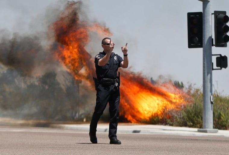 Image: A police officer turns traffic away as flames leap behind him in Carlsbad, Calif.