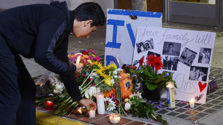 Image: A man places a candle at a makeshift memorial next to the Isla Vista Deli Mart