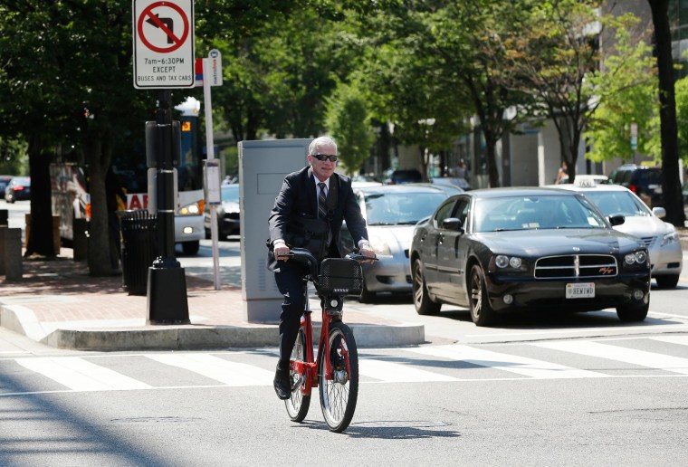 Image: A man wearing suit uses a Capital Bikeshare (CaBi) during rush hour in downtown Washington
