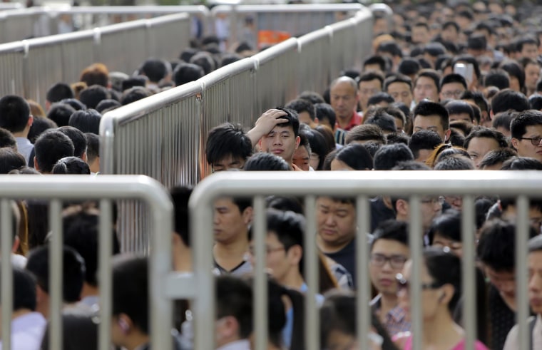 Image: A man looks up as he lines up with other passengers and waits for a security check during morning rush hour at Tiantongyuan North Station in Beijing