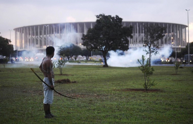 Image: Native Brazilian stands in front of the Mane Garrincha soccer stadium as police use tear gas in Brasilia