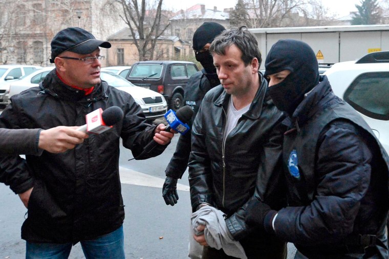 Image: Lehel, alleged hacker "Guccifer", is escorted by masked policemen in Bucharest, after being arrested in Arad