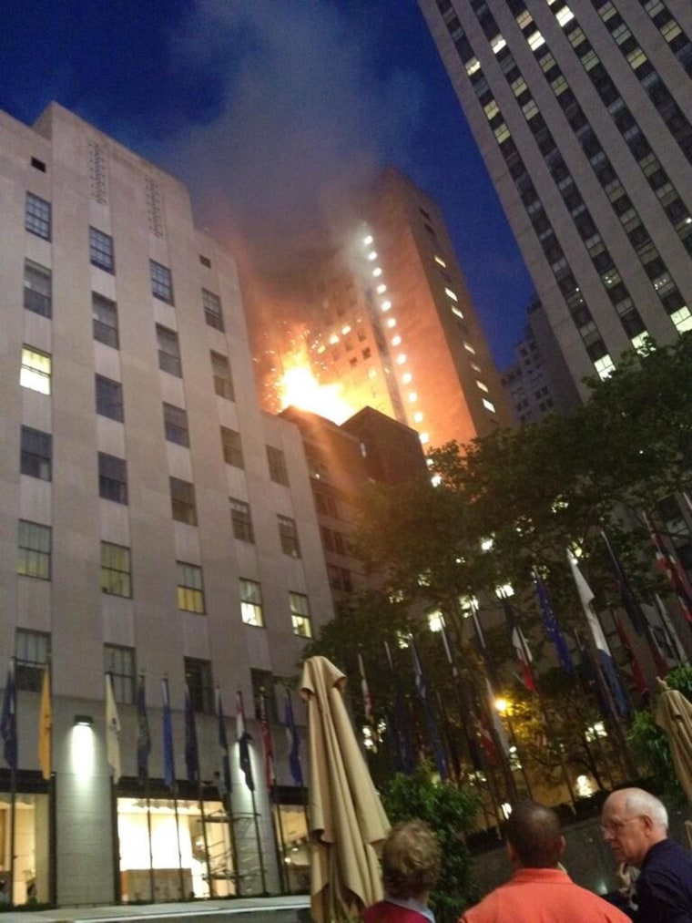 Image: Heavy smoke and flames are seen shooting from the top of a building on Fifth Avenue across from Rock Center