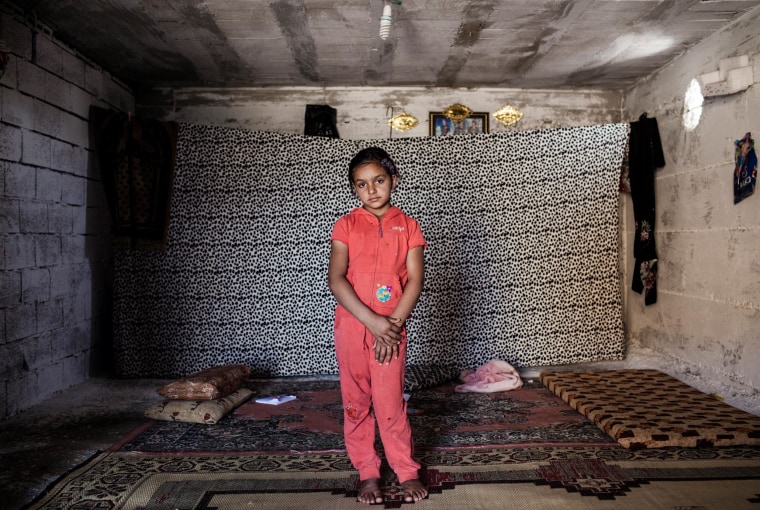 Image: Najua, 9, stands in the tiny shop front room where she lives with her mother Meyada and two brothers in Reyhanli, Turkey.