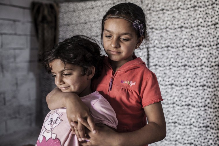 Image: Najua and her younger sister Iman, 6, stand in the tiny shop front room where they live with their mother Meyada and two brothers in Reyhanli, Turkey.