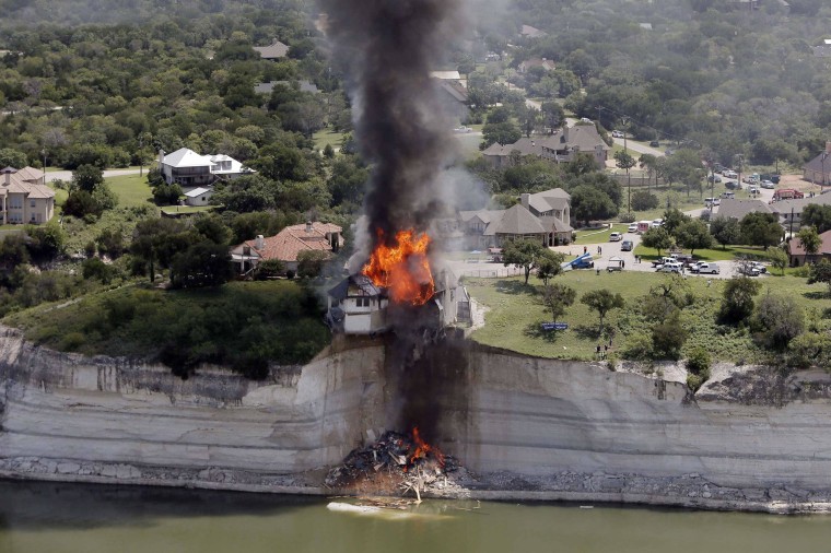 Image: Smoke rises from a house deliberately set on fire, days after part of the ground it was resting on collapsed into Lake Whitney