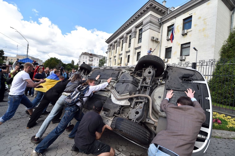 Image: People flip a car over during a rally against the Russian president in front of the Russian embassy in Kiev