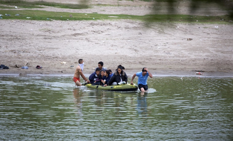 Image: Two guides lead a raft full of migrants across the Rio Grande