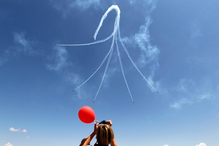 Image: A woman watches as Latvia's Baltic Bees aerobatic team on L-39C Albatross airplanes, perform a maneuver during Bucharest International Air Show at Baneasa airport