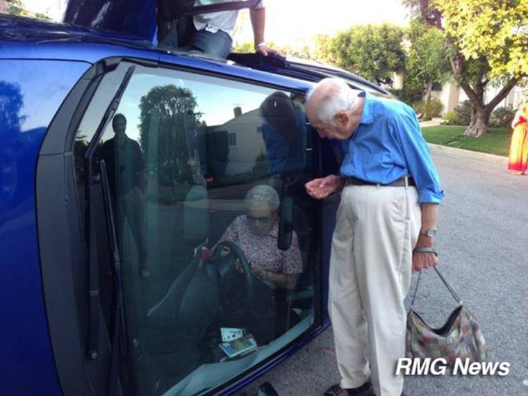Image: An elderly couple poses with their flipped car